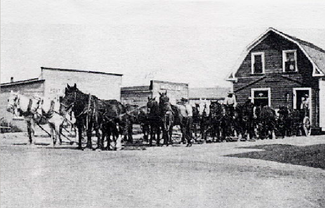 A train is stopped in a small town next to a train station and two elevators.