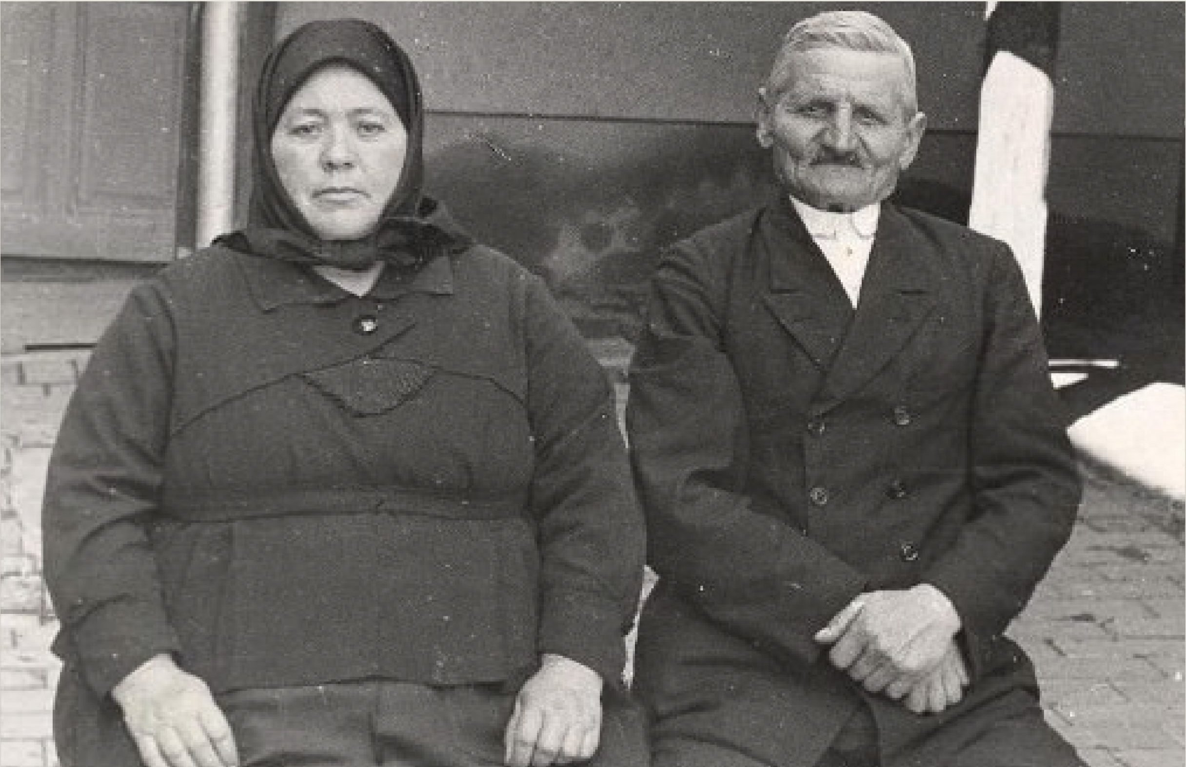 n older Hungarian couple sit on a sidewalk together.