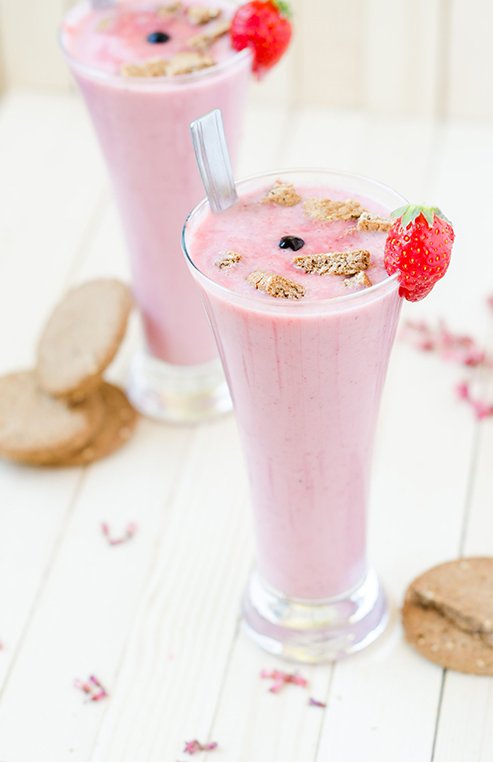 A close-up of pink-coloured strawberry smoothie has a strawberry on the rim of the glass.