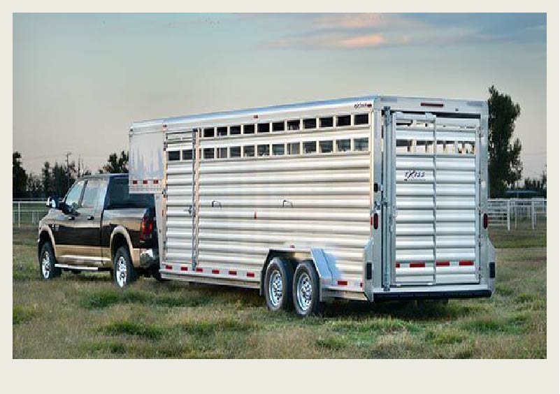 A cattle trailer is hooked up to a truck and parked in a field.