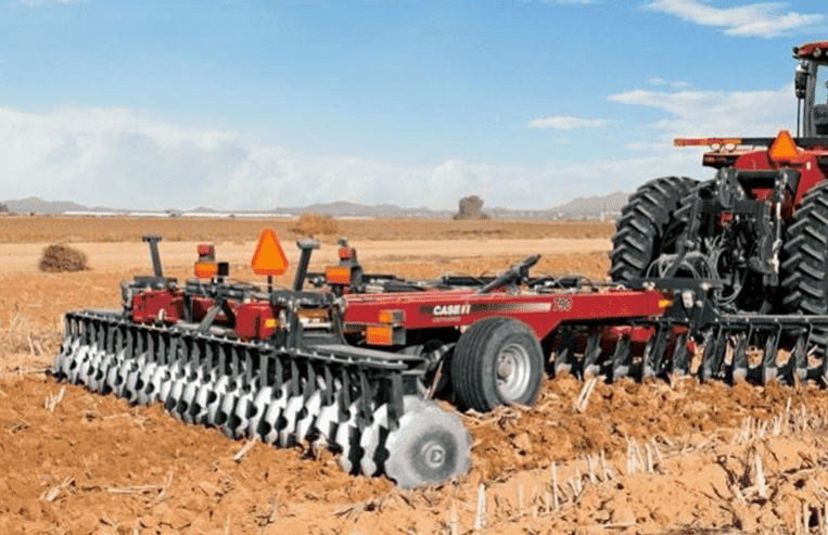 A tractor pulls modern diskers through a farm field. 