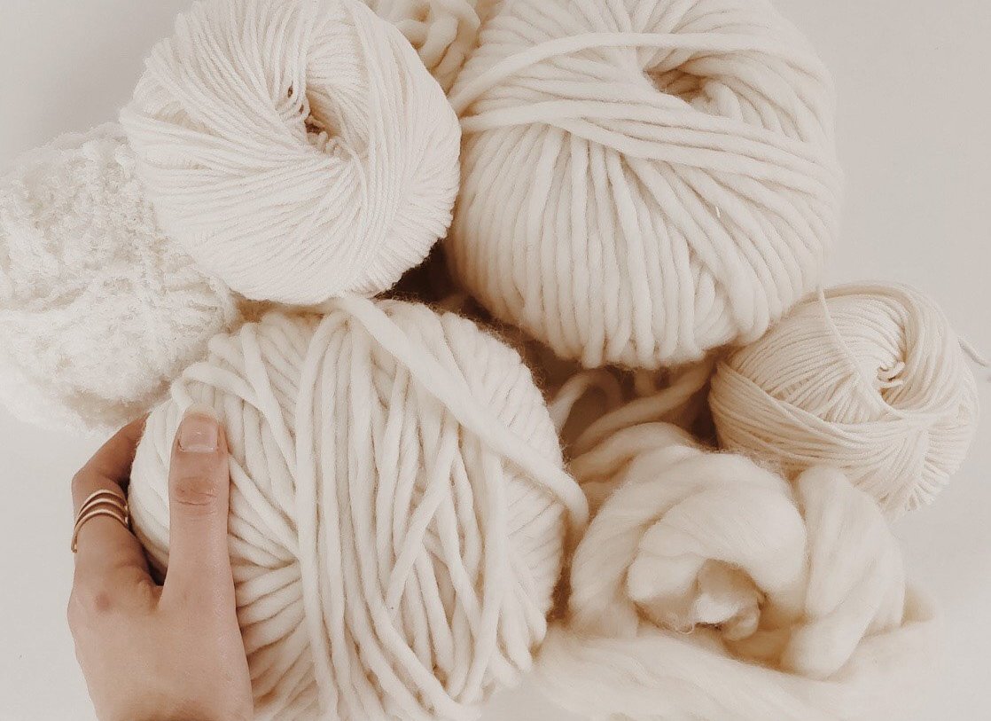 A hand is reaching out and grabbing a roll of yarn from a pile of different sized spools.