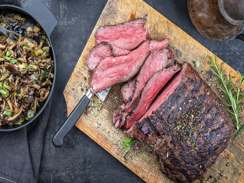 A llama roast sits half cut on a wooden platter on a counter.