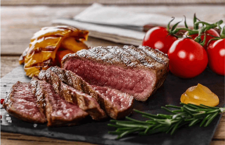 Elk meat next to tomatoes and spices on a wooden platter.