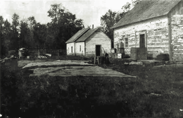 Two wooden buildings stand next to each other with a garden nearby.