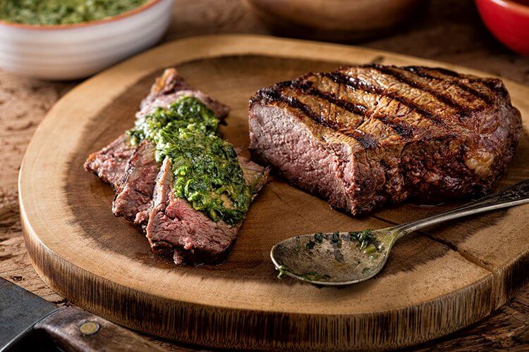 A grilled llama ribeye steak sits next to vegetables on a plate.