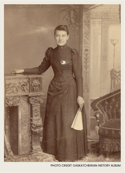 A woman in a nice dress is standing inside of a house, next to a fireplace. 