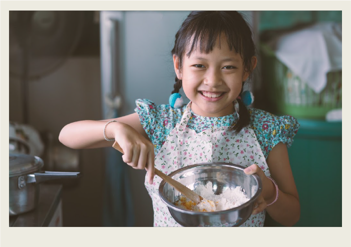 A girl is holding a bowl that has baking ingredients in it as she stirs it. 