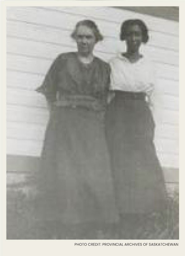 Two young African Canadians women are standing in front of a wooden building for a photo.