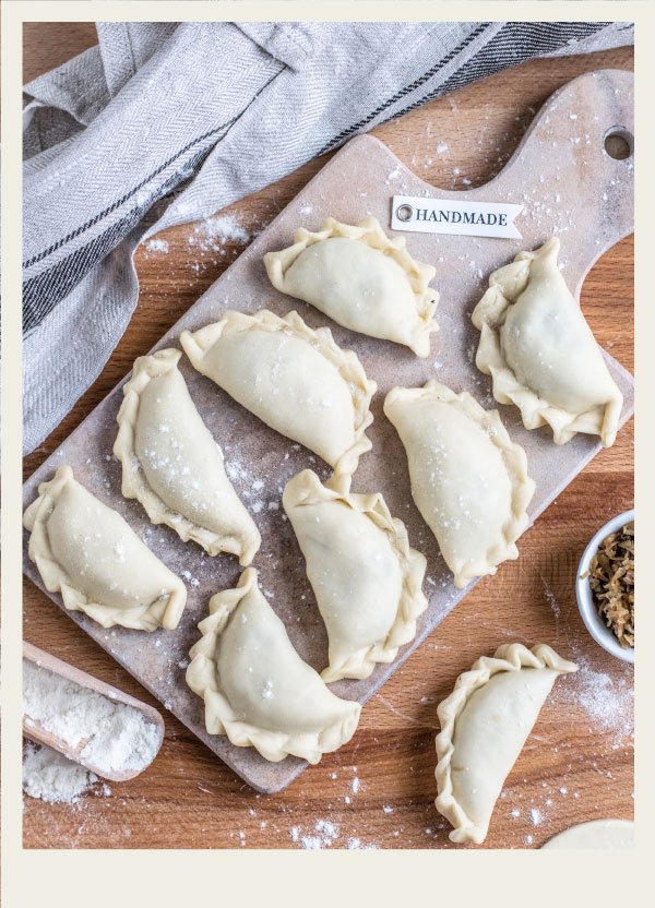 A wooden tray of homemade, uncooked perogies are shown on a table.